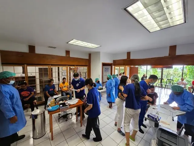 Busy clinic room with volunteers in blue gowns and patients during a community clinic day