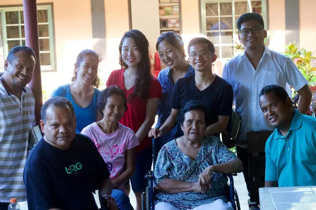 Group of volunteers and community members smiling together, one elder in a wheelchair