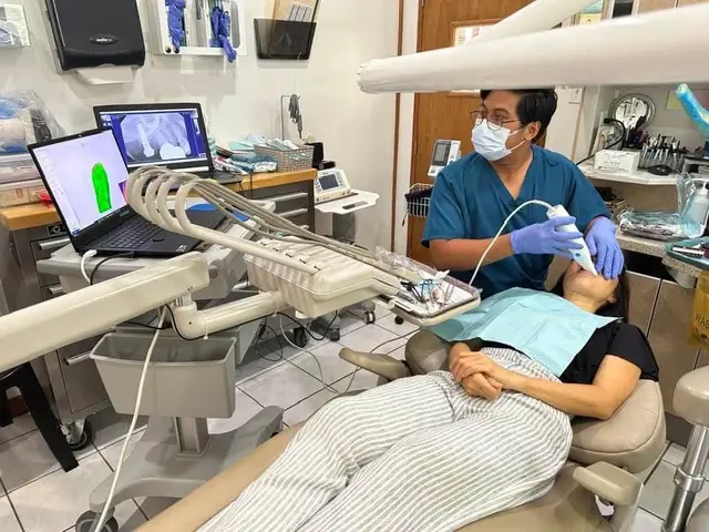 Dentist taking a digital X-ray of a patient while the image shows on a laptop