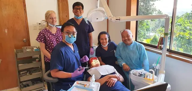 Smiling dental team in scrubs around a patient in the dental chair