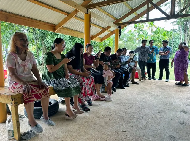 Families seated on benches under a covered outdoor shelter waiting to be seen