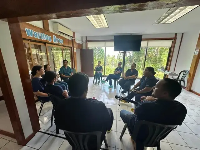 Patients seated in the clinic waiting area with windows onto the forest
