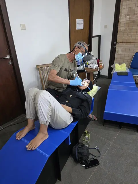 A volunteer dentist cleaning a young woman’s teeth on a portable bed