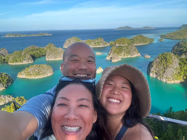 Three team members smiling in a selfie above the turquoise karst islands of Raja Ampat