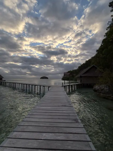 Wooden jetty leading out over clear water at dawn under a cloudy sky