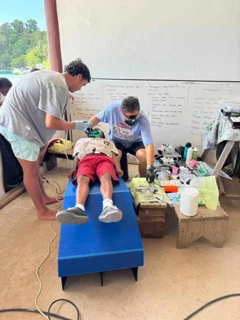 Two volunteers treating a schoolboy lying on a blue portable dental bed