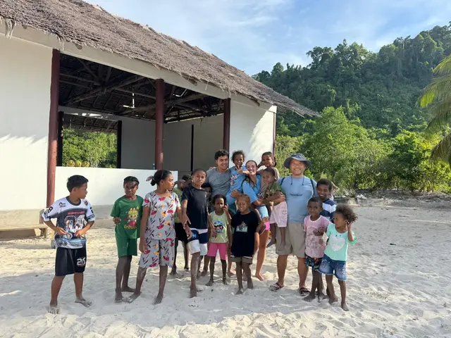 Team members on a sandy beach surrounded by smiling local children