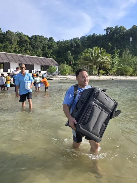 Volunteers wading ashore from the boat carrying suitcases and boxes of supplies