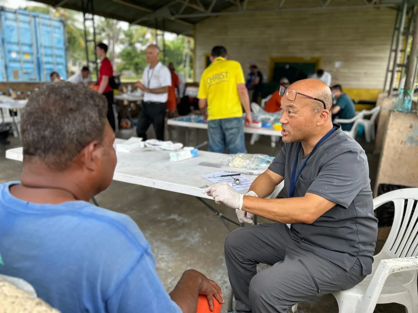 Dr. Steve Chang consulting with a patient at a table in an outdoor clinic shelter