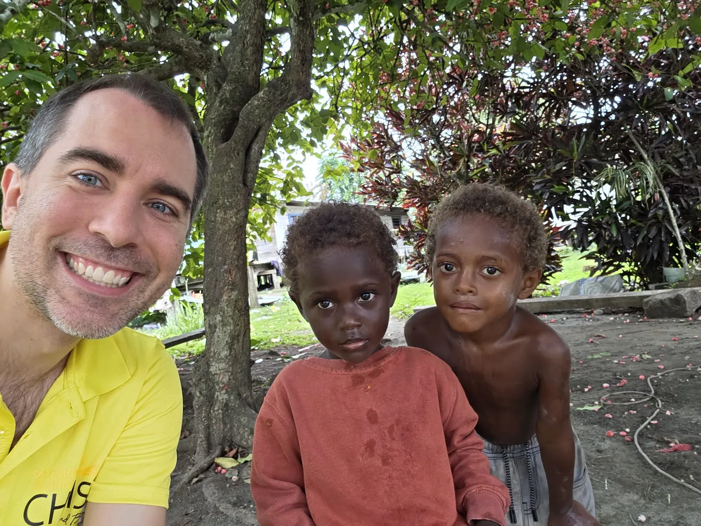 Tom taking a selfie with two children from the Solomon Islands under a tree
