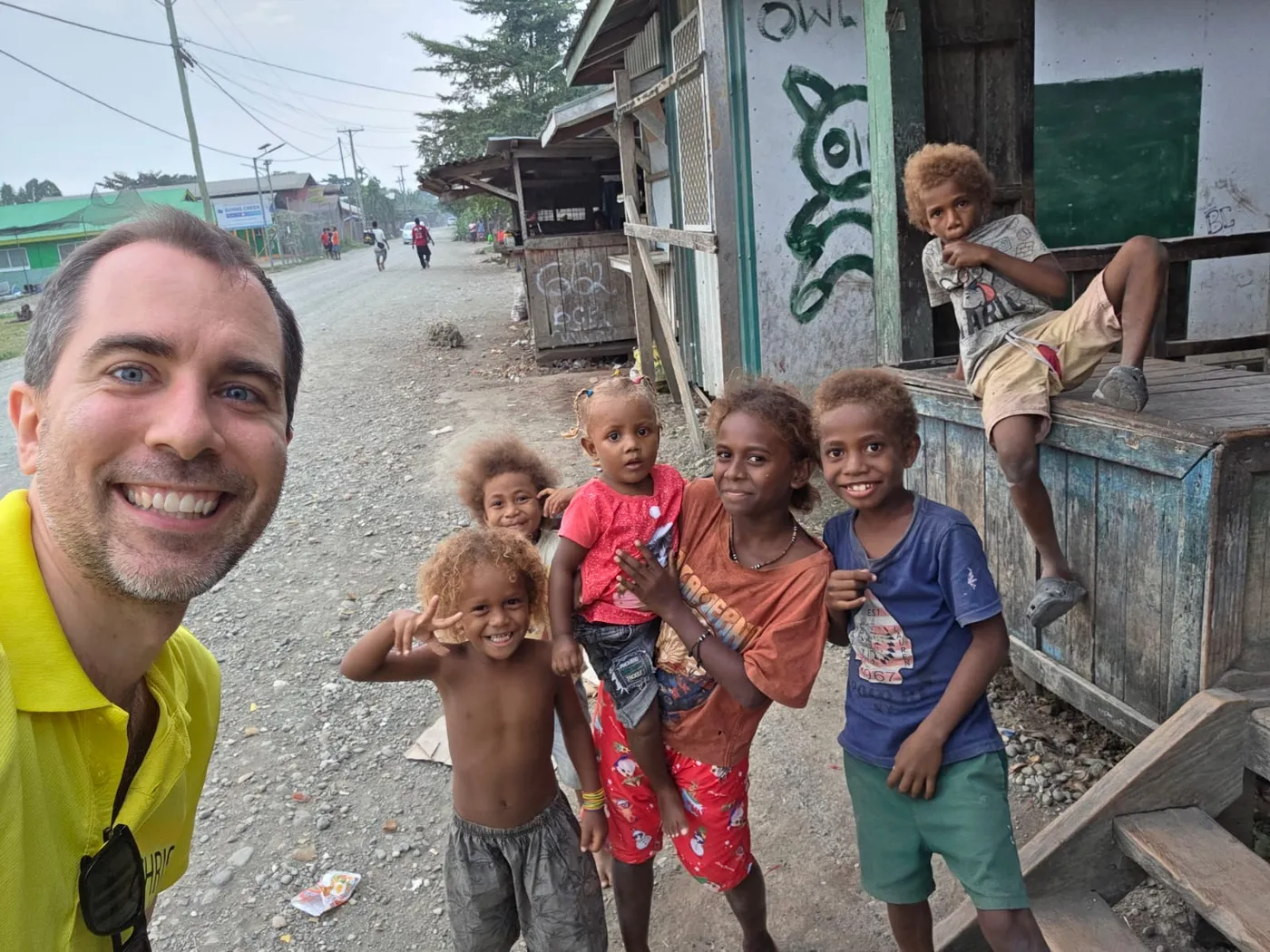Tom Sliwa smiling in a selfie with a group of young children from the Solomon Islands on a village street